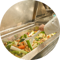 Ein Koch kocht Gemüse in einem großen Lavur Ein Koch kocht Gemüse in einem großen Lavur